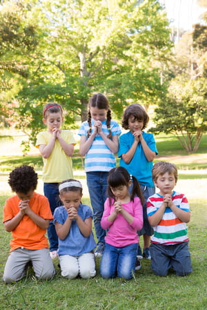 Children saying their prayers in park on a sunny day
