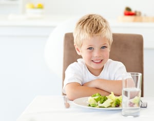 Cute little boy with his salad for lunch sitting at a table in the kitchen