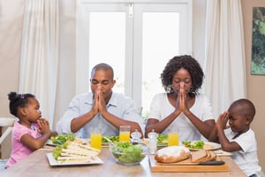 Happy family saying grace before meal at home in the kitchen